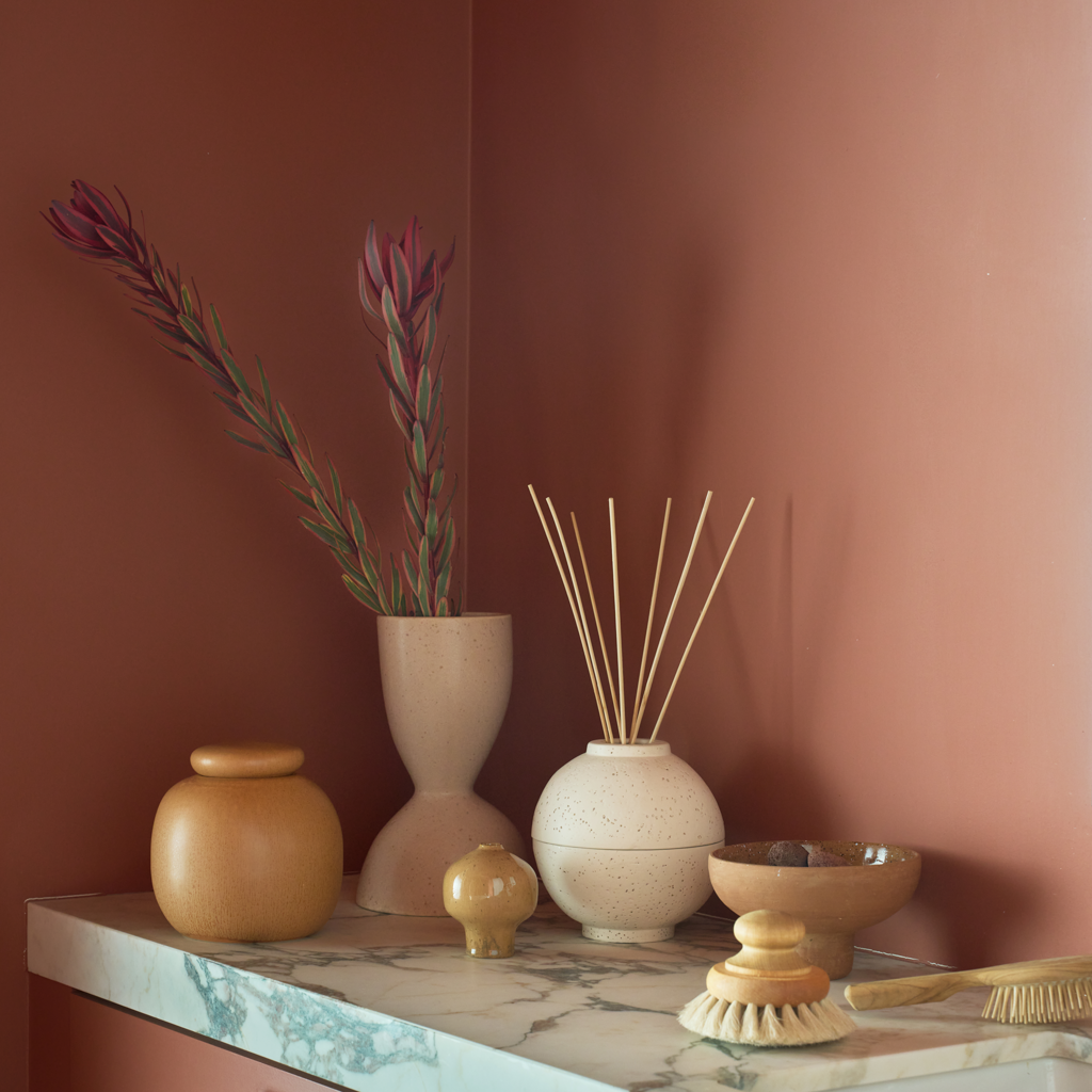 Kiri diffuser holder with reeds styled against a terracotta wall with vases