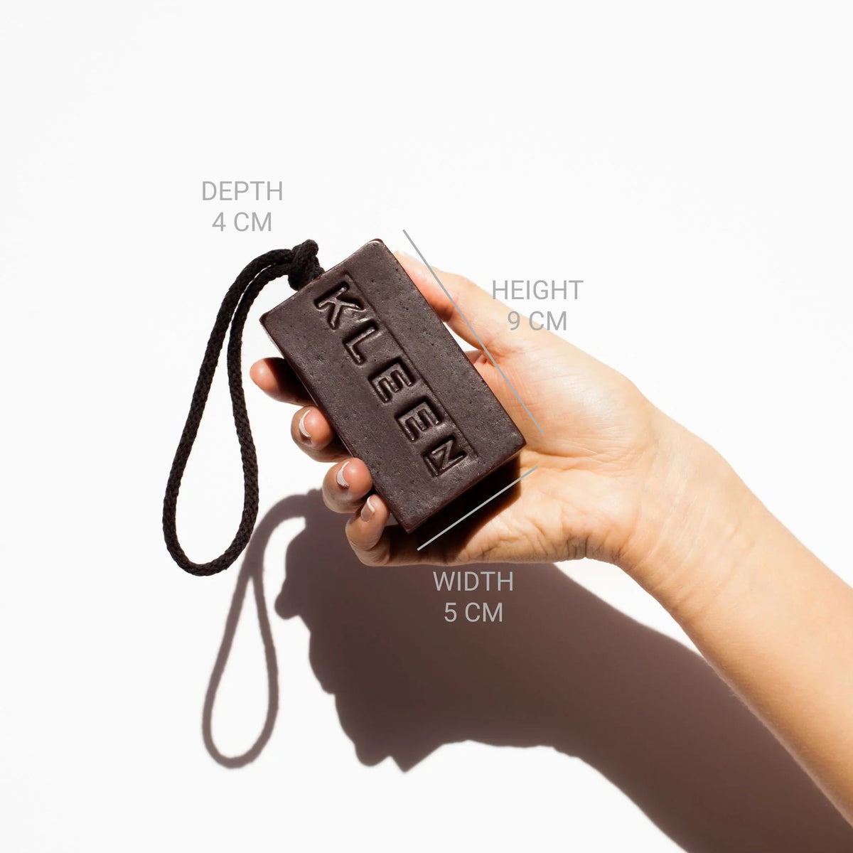 Hand holding the KLEEN Tall Dark and Handsome soap bar with dimensions marked to show its size
