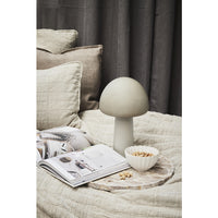 Beige marble tray on a linen bed with a small bowl, an open magazine and a mushroom lamp