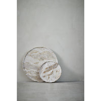 Two Ellia round beige marble trays propped against a grey plaster wall