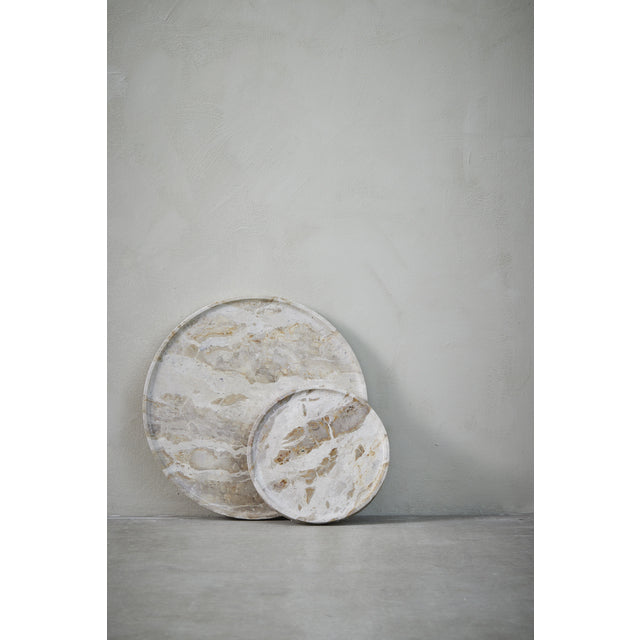 Two Ellia round beige marble trays propped against a grey plaster wall