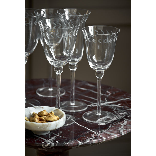 Etched wine glasses and a bowl of nuts on the burgundy marble top of the Marel side table