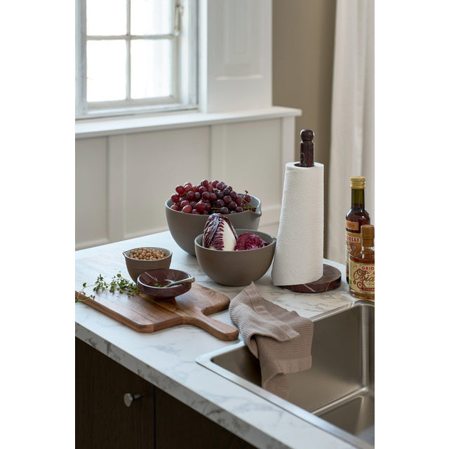 Burgundy marble kitchen roll holder on a kitchen worktop beside bowls of fruit and a chopping board