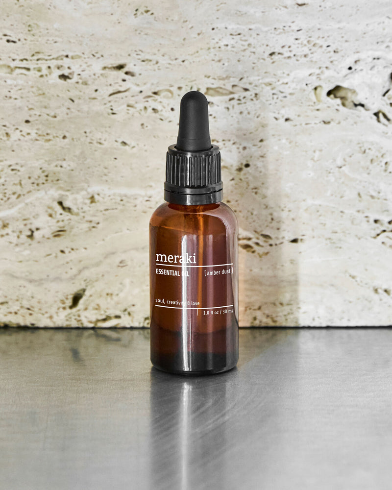 Meraki Amber Dust essential oil bottle on a steel surface against a travertine wall