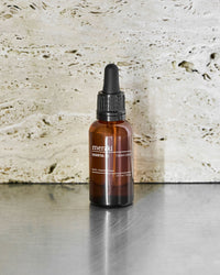 Meraki Herbal Calm essential oil bottle on a steel surface against a travertine wall