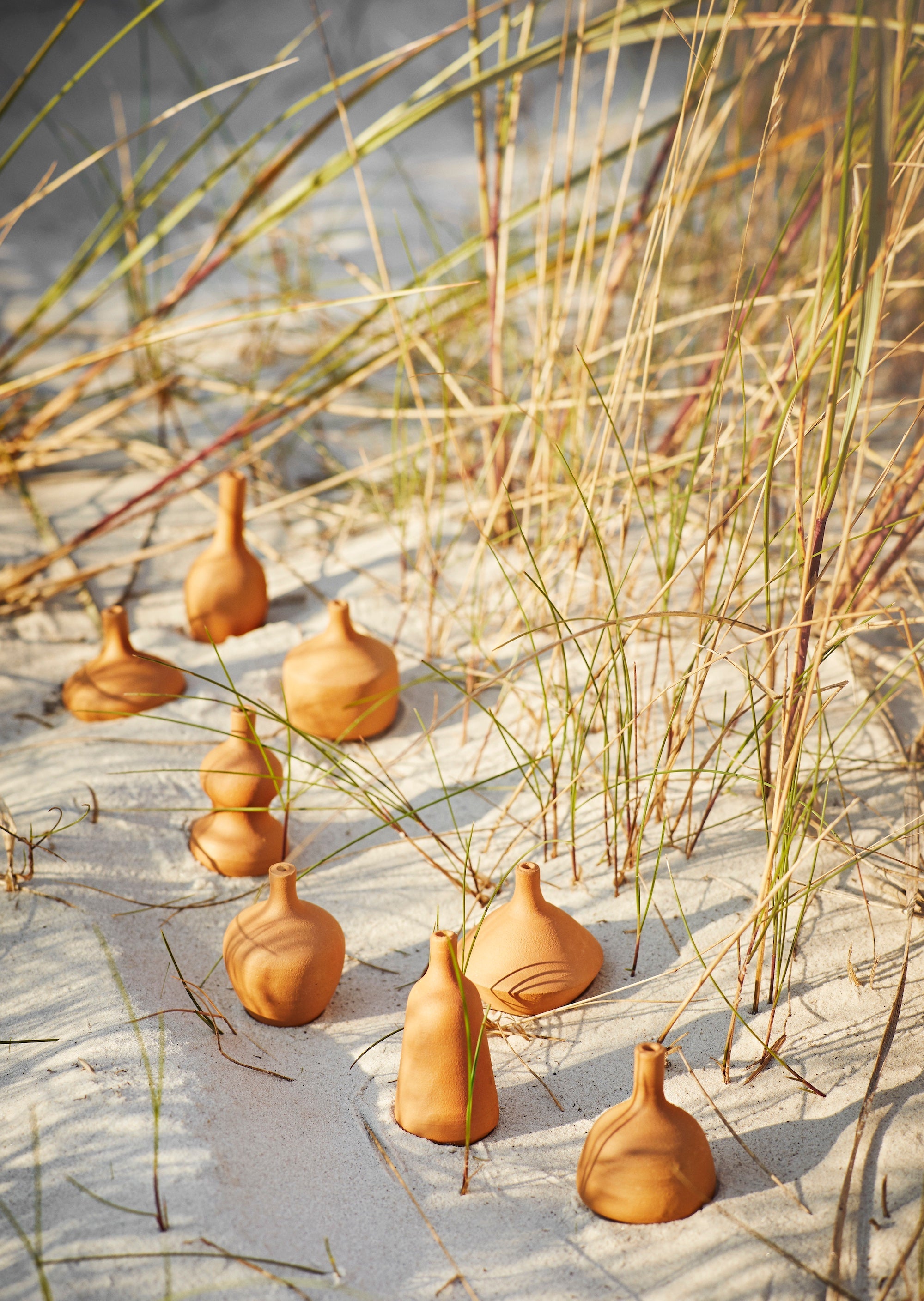 terracotta mini vases scattered on sand for a rustic, natural display
