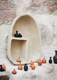 Collection of small ceramic vases in various colors against a textured stone wall.