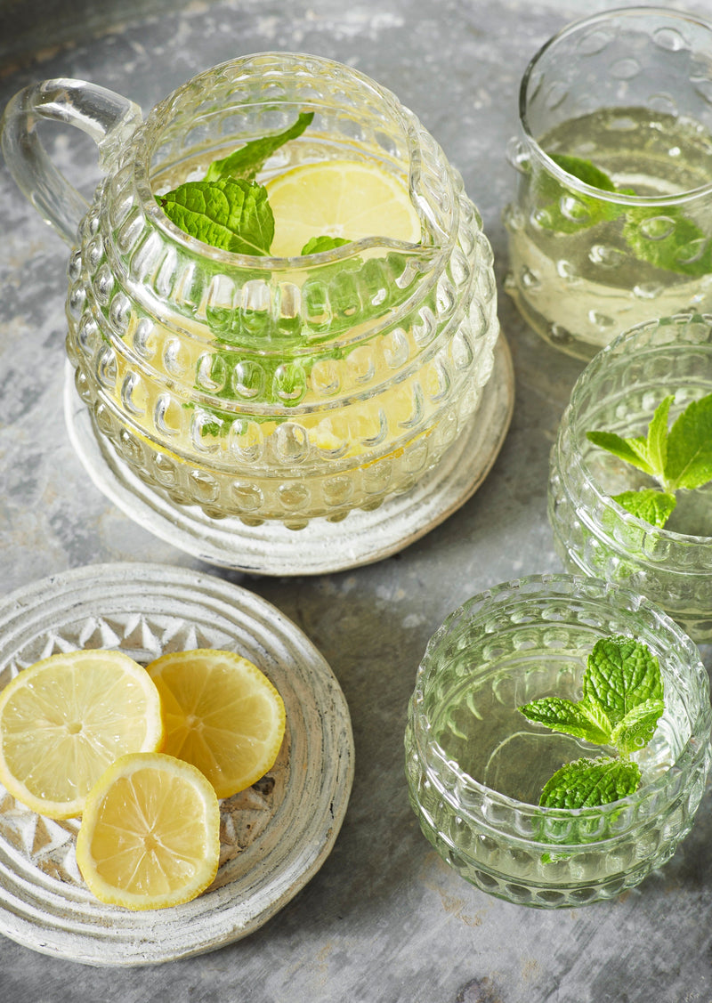 clear dotted drinking glasses and matching jug with lemon and mint on a table
