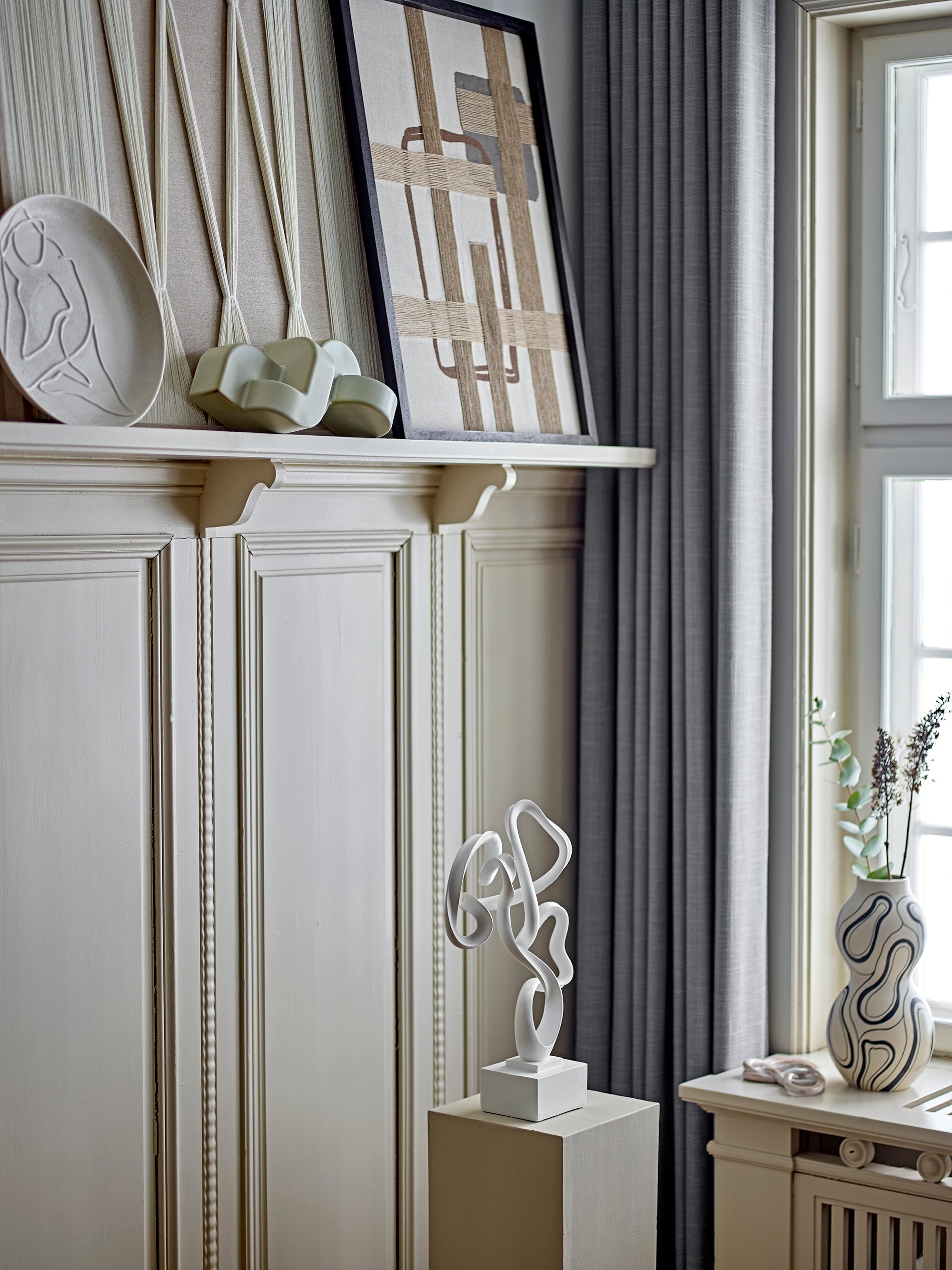 Large sculptural vase with black line pattern styled on mantel with modern artwork