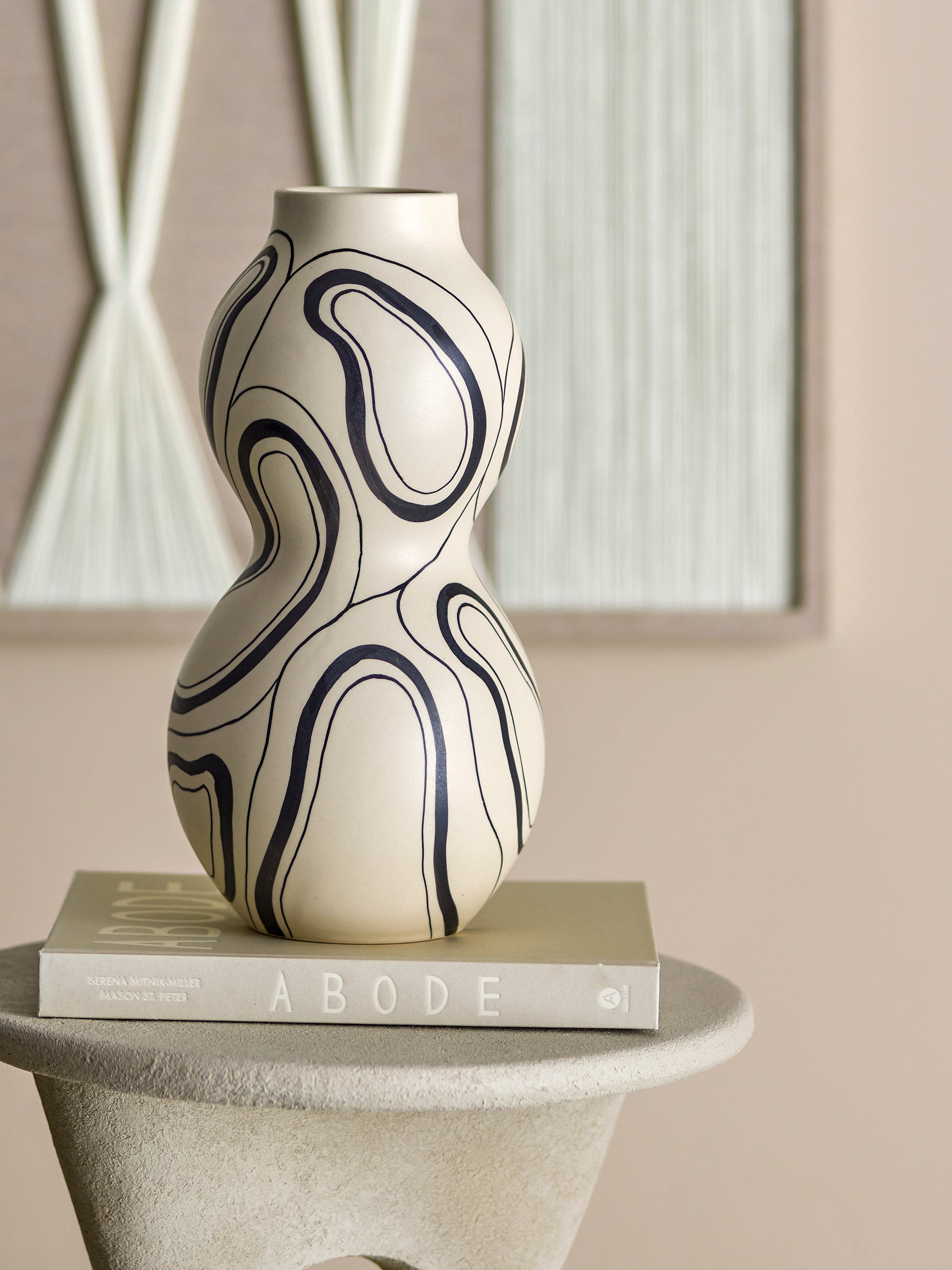 Organic black line vase displayed on neutral pedestal with art book
