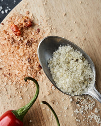 Spoonful of Nicolas Vahé Parmesan and basil salt beside chilli salt and a red chilli on a wooden board