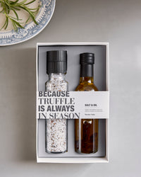 Nicolas Vahé truffle salt and oil gift box on a grey table beside a patterned plate and fresh herbs