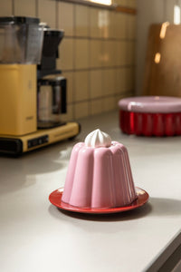Pink pudding cloche on a red plate styled on a kitchen counter