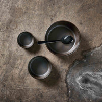raw metallic brown bowl set by aida styled on a textured table with matching stoneware pieces
