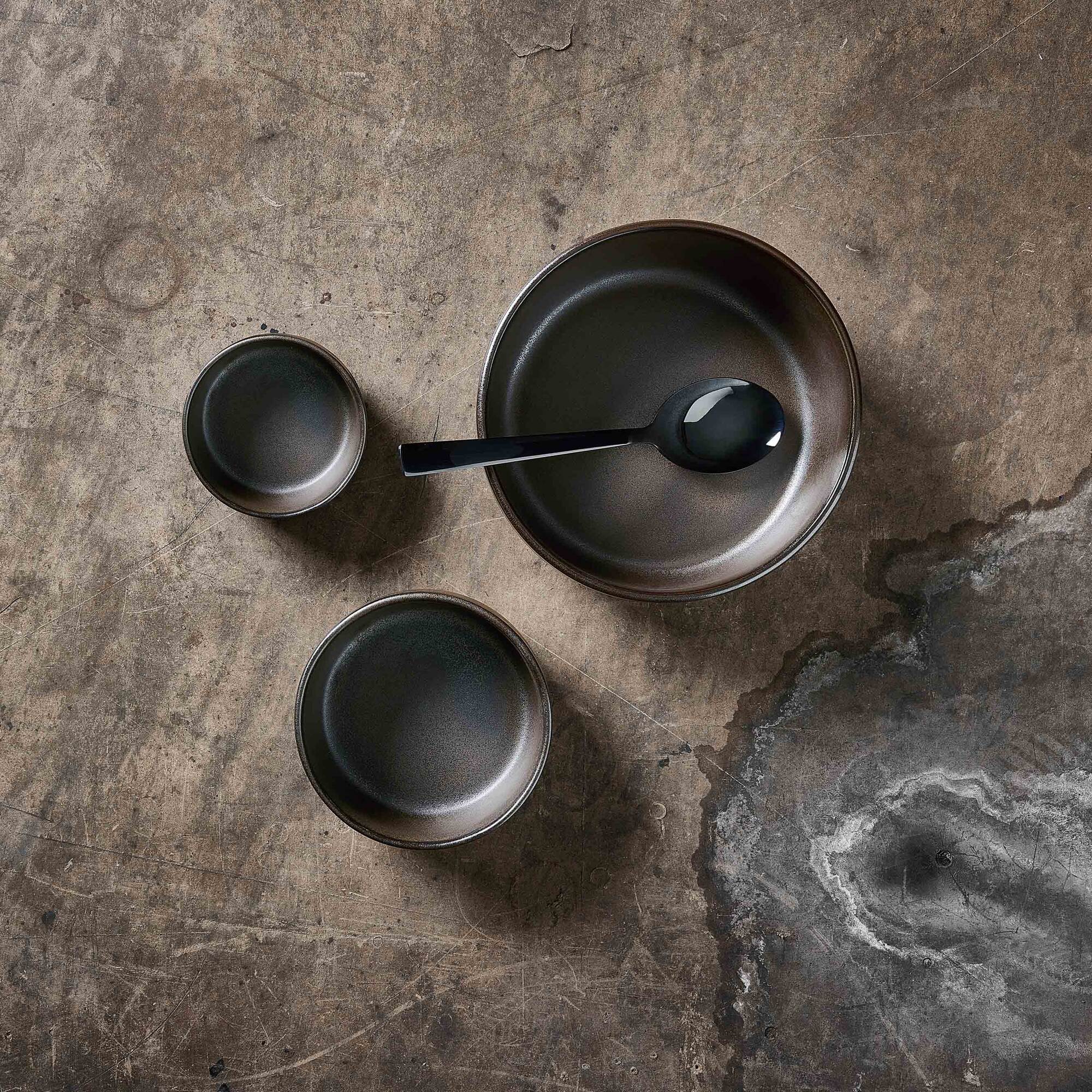 raw metallic brown bowl set by aida styled on a textured table with matching stoneware pieces
