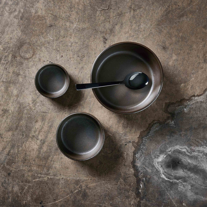 raw metallic brown bowl set by aida styled on a textured table with matching stoneware pieces
