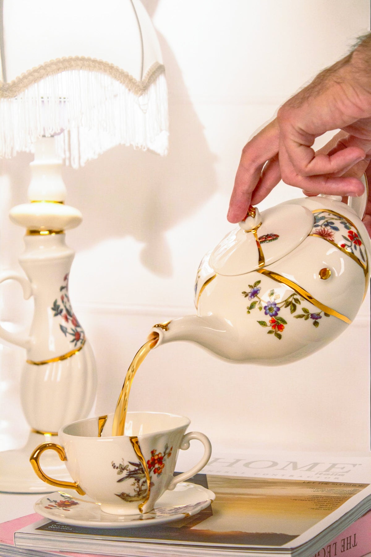 Kintsugi teapot by Seletti pouring tea into matching gold-detailed cup and saucer
