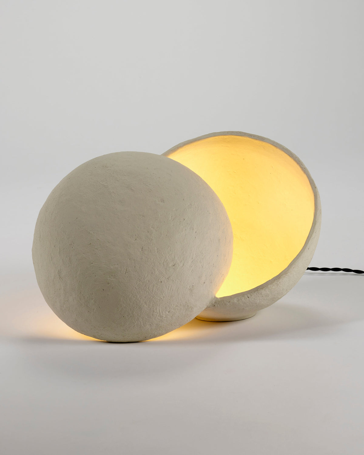 Serax Earth table lamp switched on, warm light glowing from the gap between the two paper mâché halves