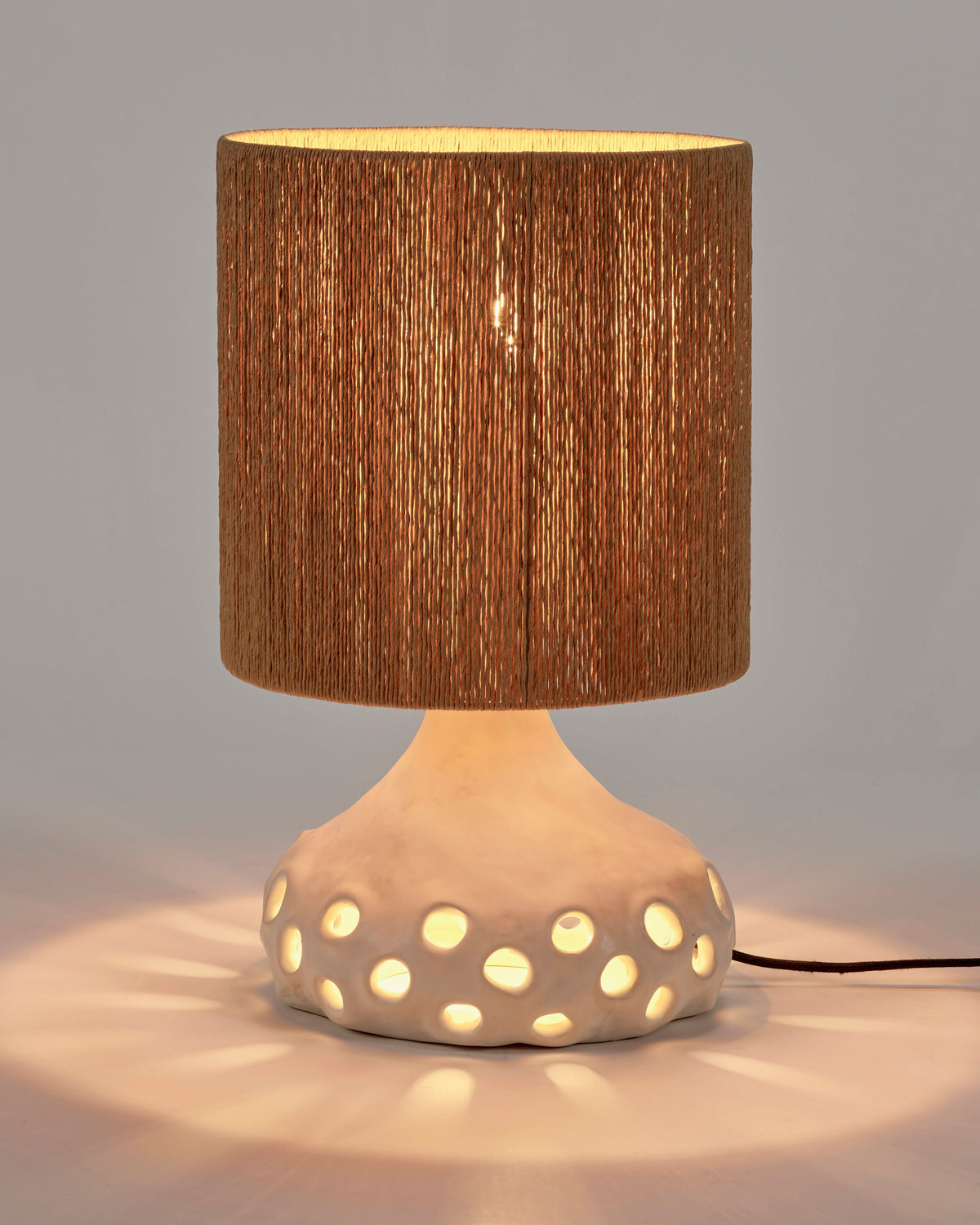 Serax Oya table lamp switched on, light glowing through the shade and dotted base