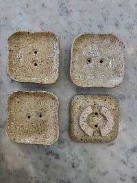Four square ceramic soap dishes with textured surface on a marble countertop