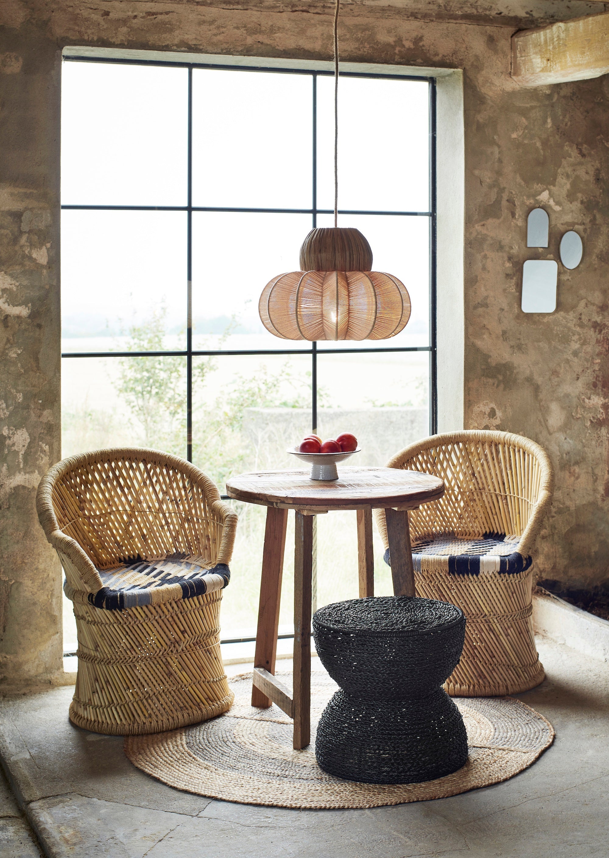 Rattan chairs and a small table with a decorative lamp in a room with large windows.