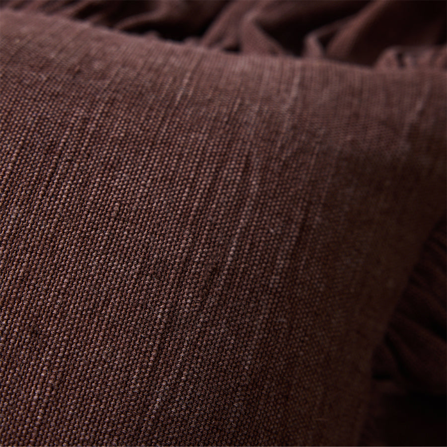 Close-up of woven cotton texture and ruffled trim on chestnut brown cushion
