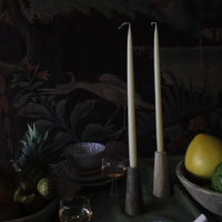 Travertine candle holders by Olsson & Jensen with tall taper candles on a dark table