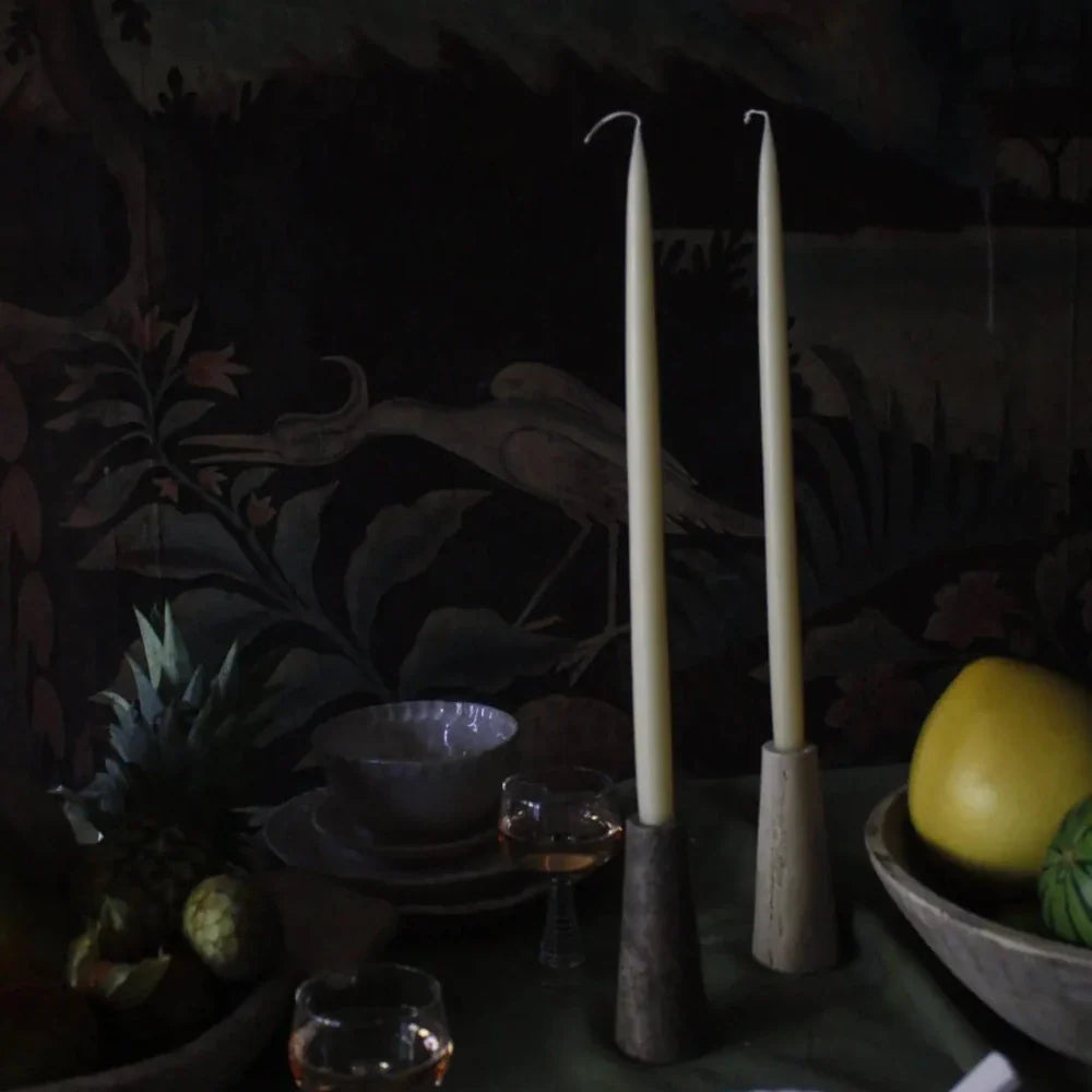 Travertine candle holders by Olsson & Jensen with tall taper candles on a dark table